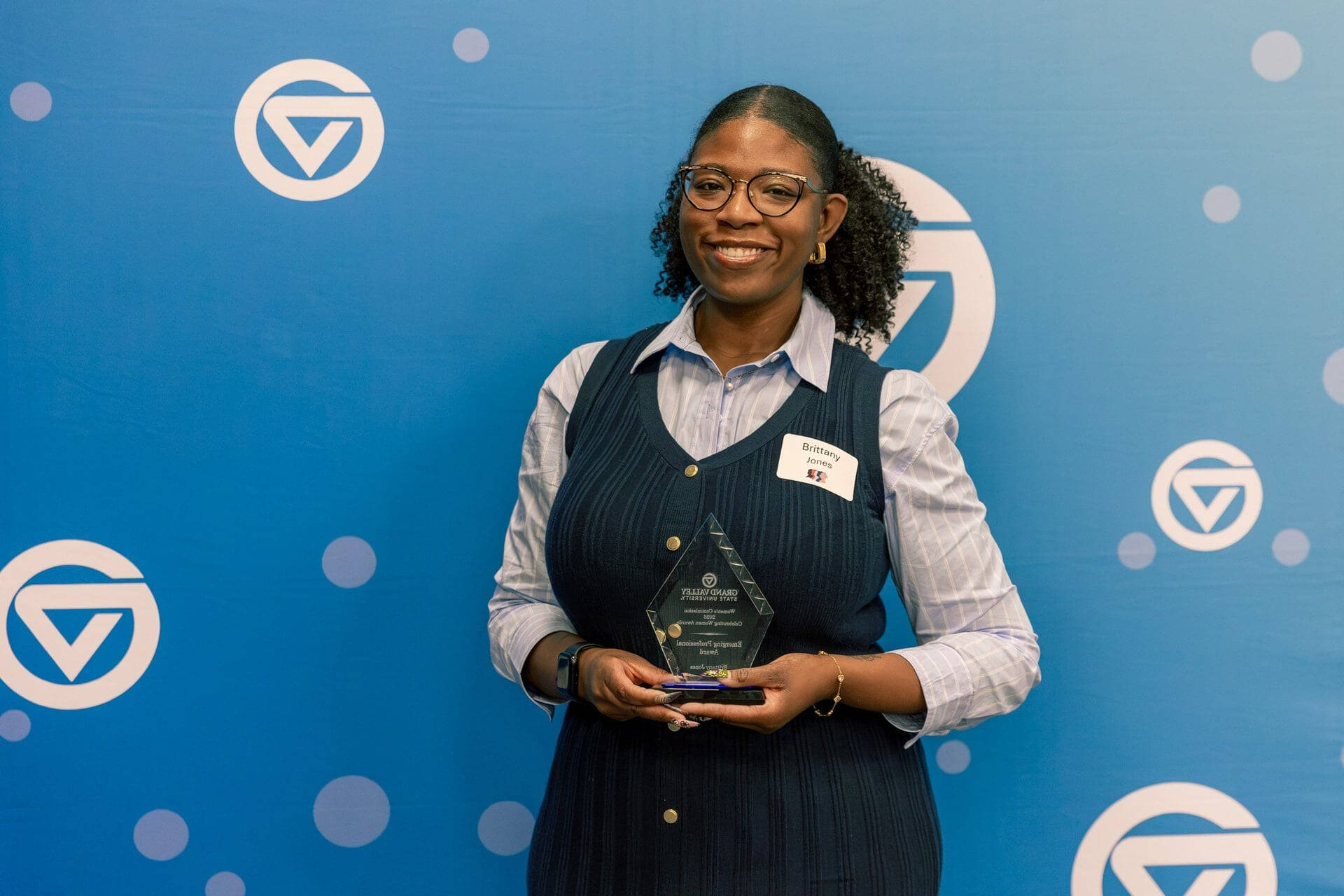 Brittany Jones holds a glass award in front of a GVSU backdrop with circle GVs